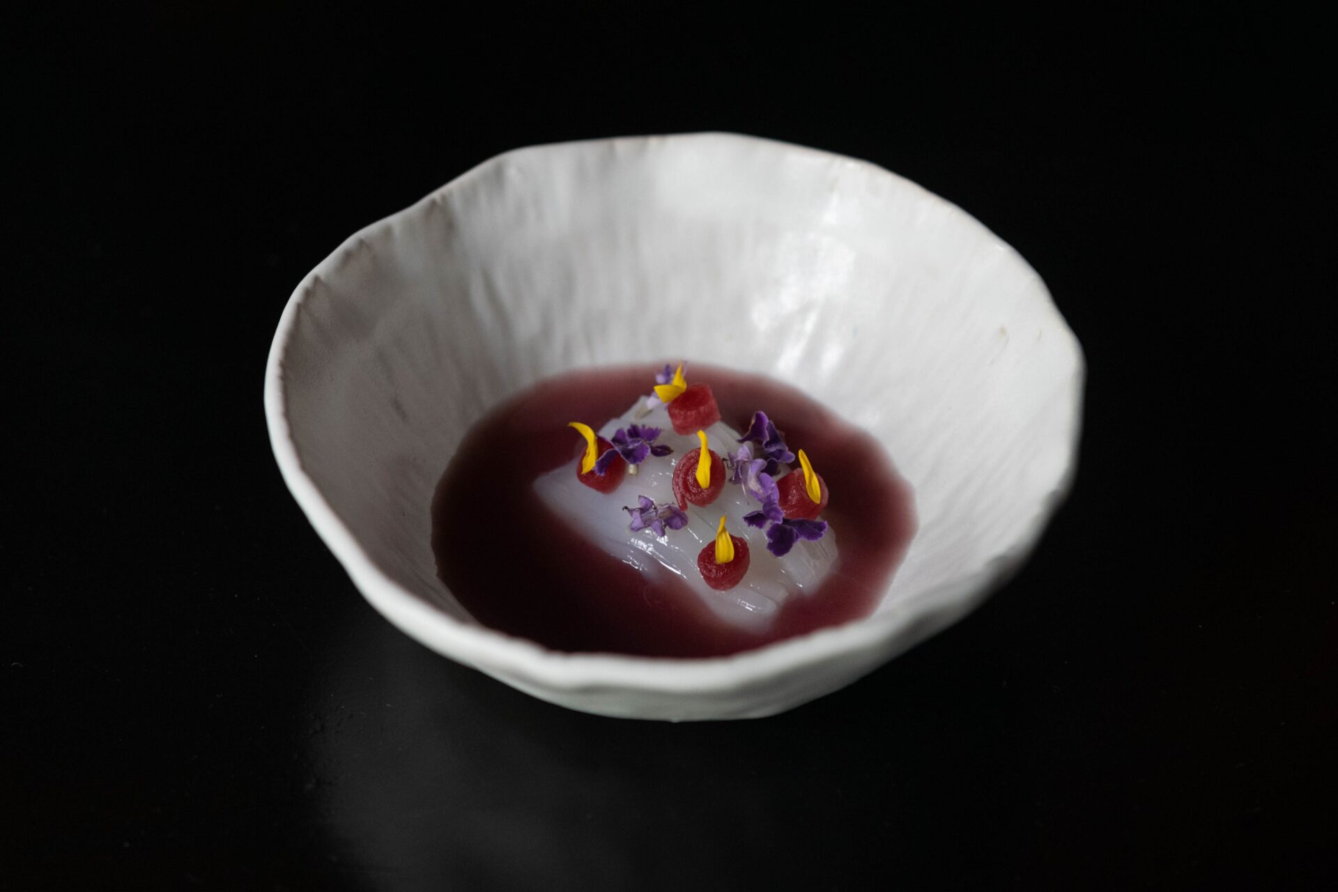 Best Bangkok restaurants | A white bowl with a dark-purple broth, a white piece of fish and delicate dark purple flowers at 80/20