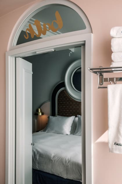 Where to stay in London | an arched doorway in a pink wall looking onto a bed with plush white sheets at Henrietta Hotel in Covent Garden