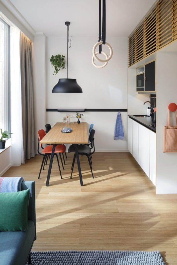 The living space at Zoku Loft, Amsterdam, with a blue sofa, a kitchenette and exercise hoops in a white-walled room with a light-wood floor