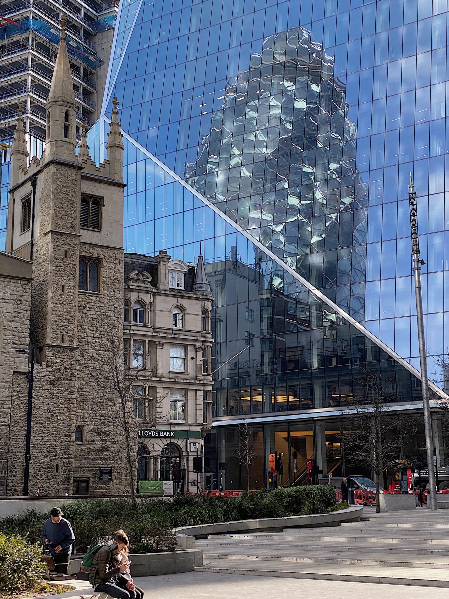 Local's guide to London | A grey brick church stands in the shadow of a mirrored building in the City of London, with the Gherkin reflected in its windows