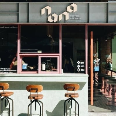 Exterior of Nana Coffee Rosters shop and co working space in Bangkok Thailand, featuring three stools by a window