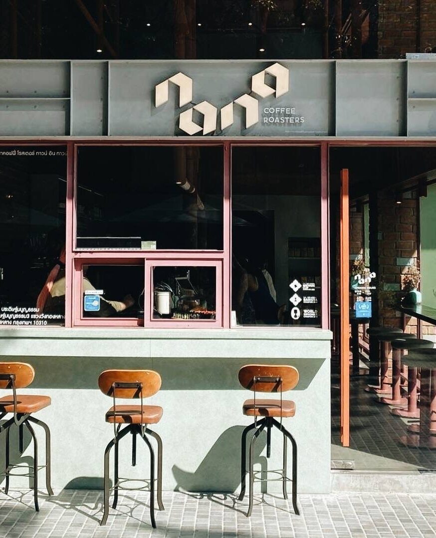 Exterior of Nana Coffee Rosters shop and co working space in Bangkok Thailand, featuring three stools by a window