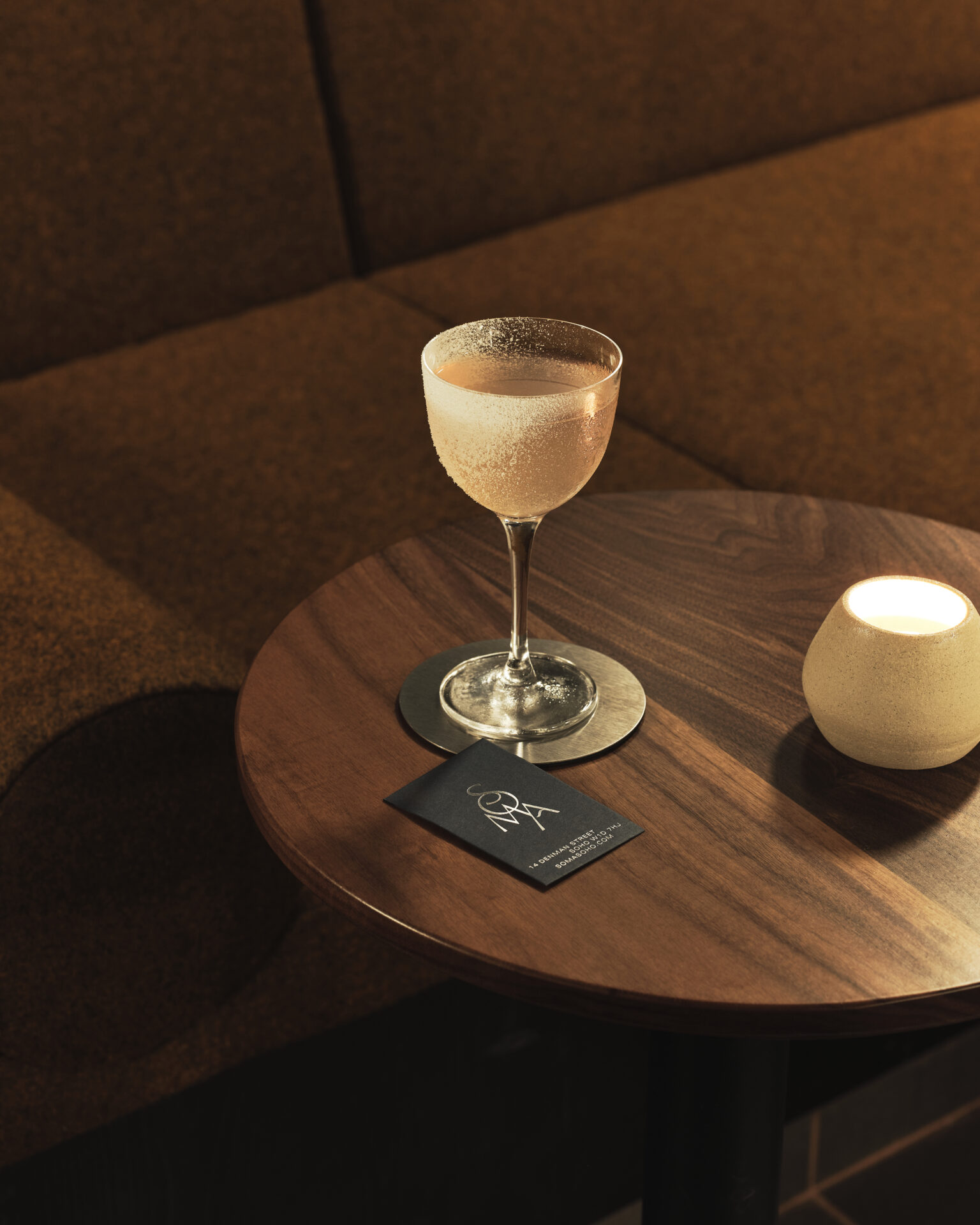 London's best cocktail bars | a pale pink cocktail on a low wooden table with a candle at Soma Soho