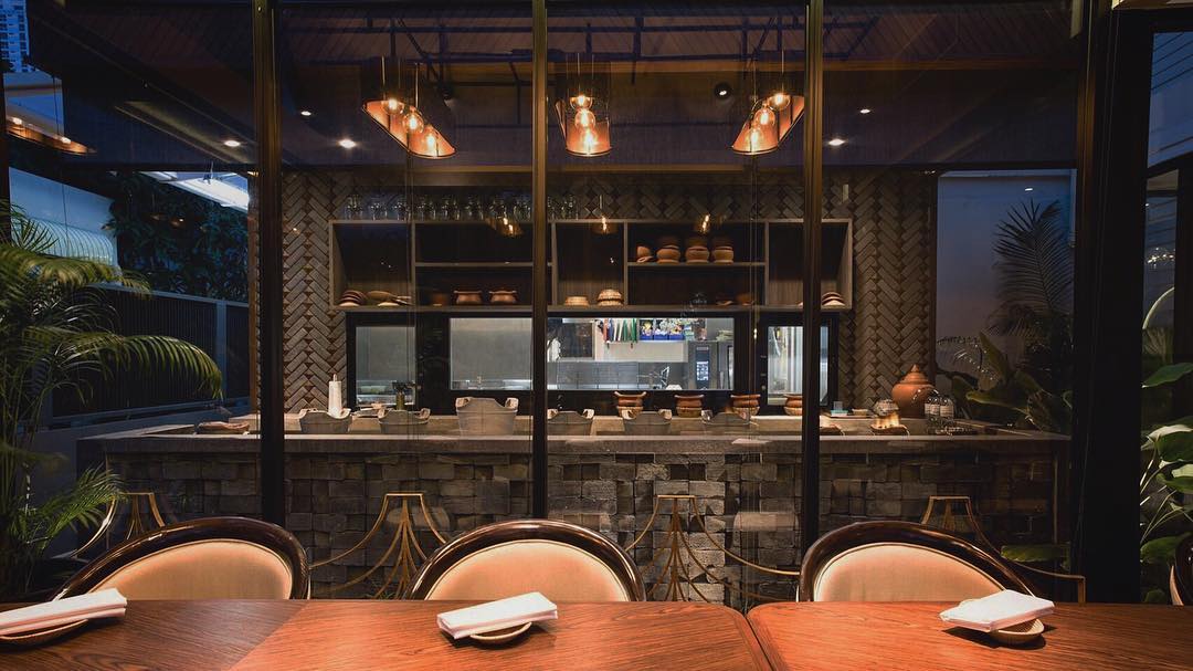 Best Bangkok restaurants | An empty table and chats stand in front of Sorn's open kitchen, with stone wall details