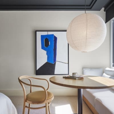 Best hotels in Shoreditch, Dalston and Hackney | A view of a bedroom in One Hundred Shoreditch. A paper light lantern hangs from the ceiling over a round table, where a wooden cane seat and a sofa can be seen. A painting hangs on the wall. The ceiling is painted in a dark grey, and the walls a light neutral shade.