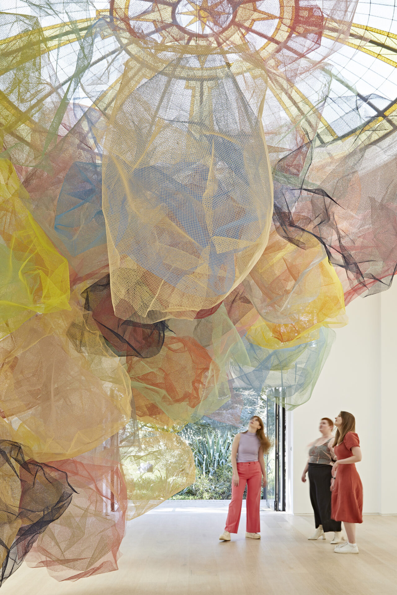 Things to do in London in June | People standing and looking up at giant coloured mesh shapes hanging from the ceiling at Rana Begum's Dappled Light exhibition