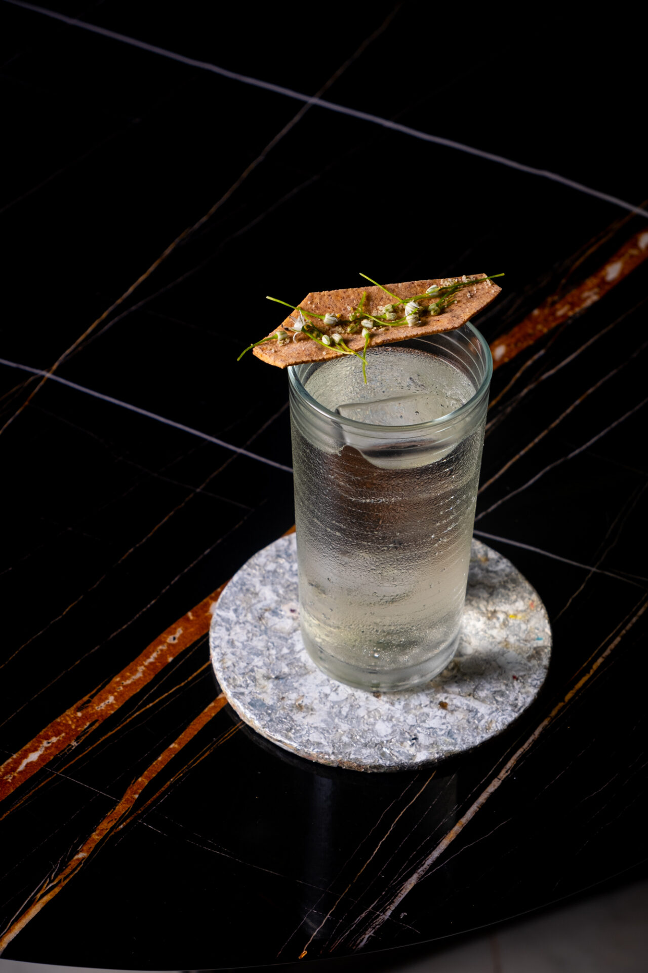 Best bars in Mumbai | A colourless cocktail served with a garnish on a black tabletop at The Living Room, Mumbai