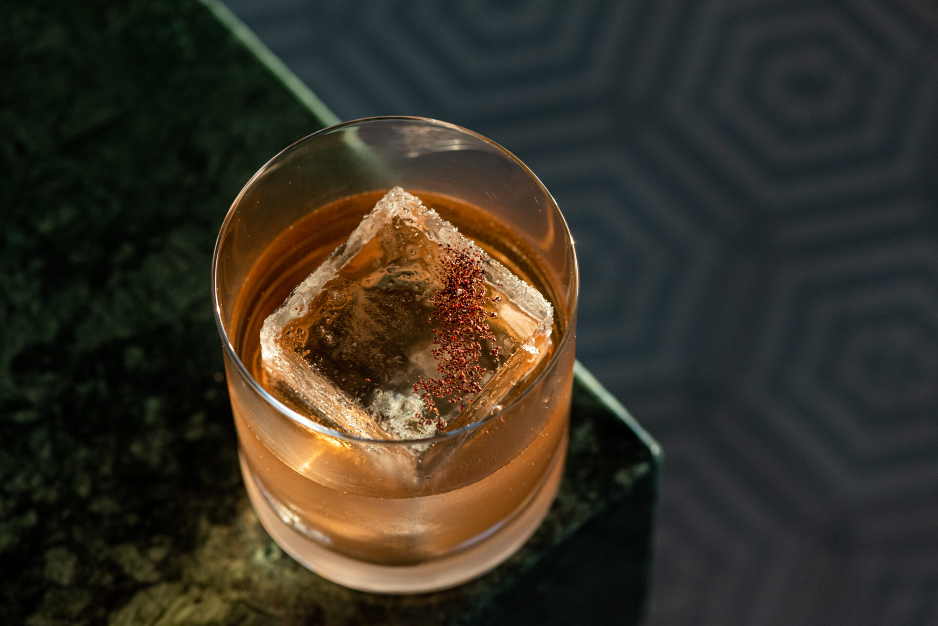 A pinky-orange liquid with a large cube of ice sprinkled with spices in a short round cocktail glass at La Cha cha cha