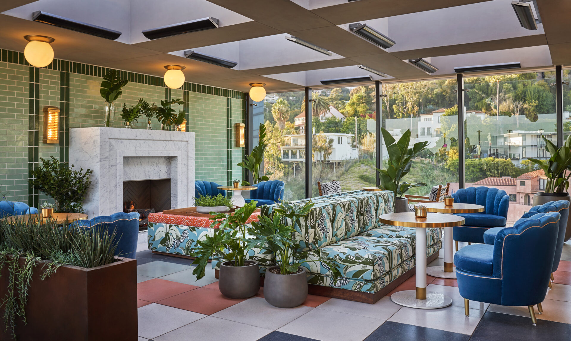 The lounge area at Merois, with palm-tree-patterned sofas, greenery and a stone fireplace under wooden beams