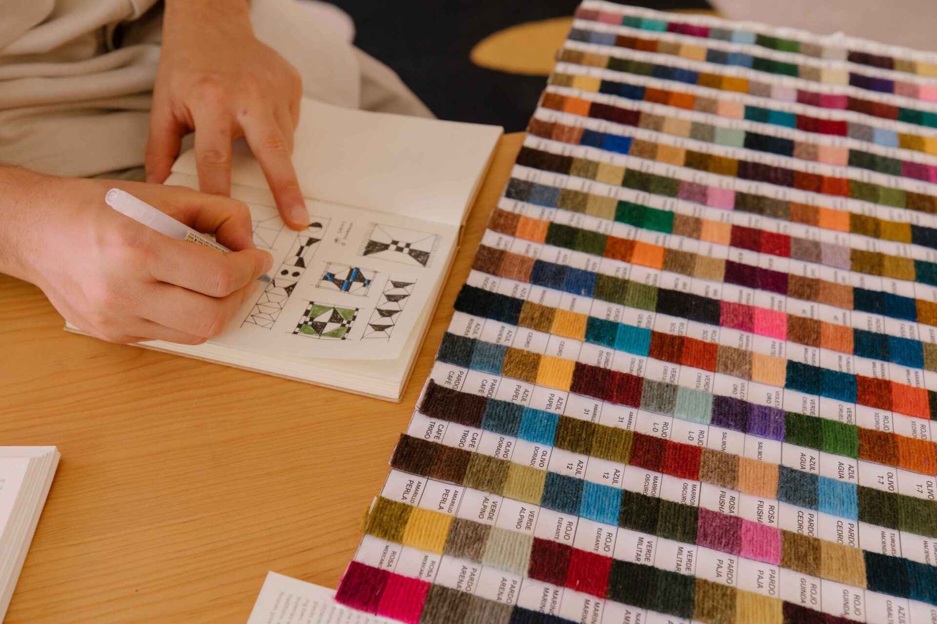 Javier Reyes, rrres studio, Oaxaca | a pair of hands holds a black pen writing in a notebook while examining a colour chart