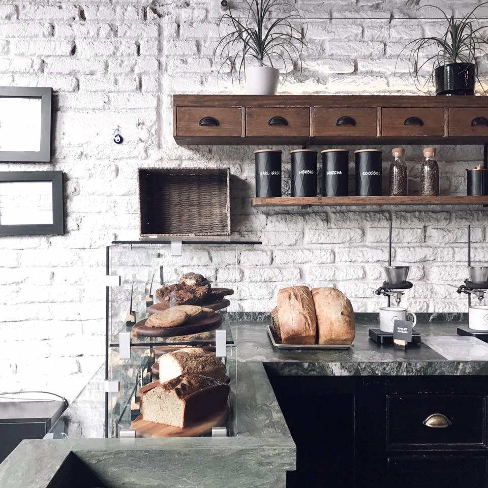 A view of the pastry counter at Dosis, with banana bread and loaves on two shelves behind a glass case, and in front of a white-painted brick wall