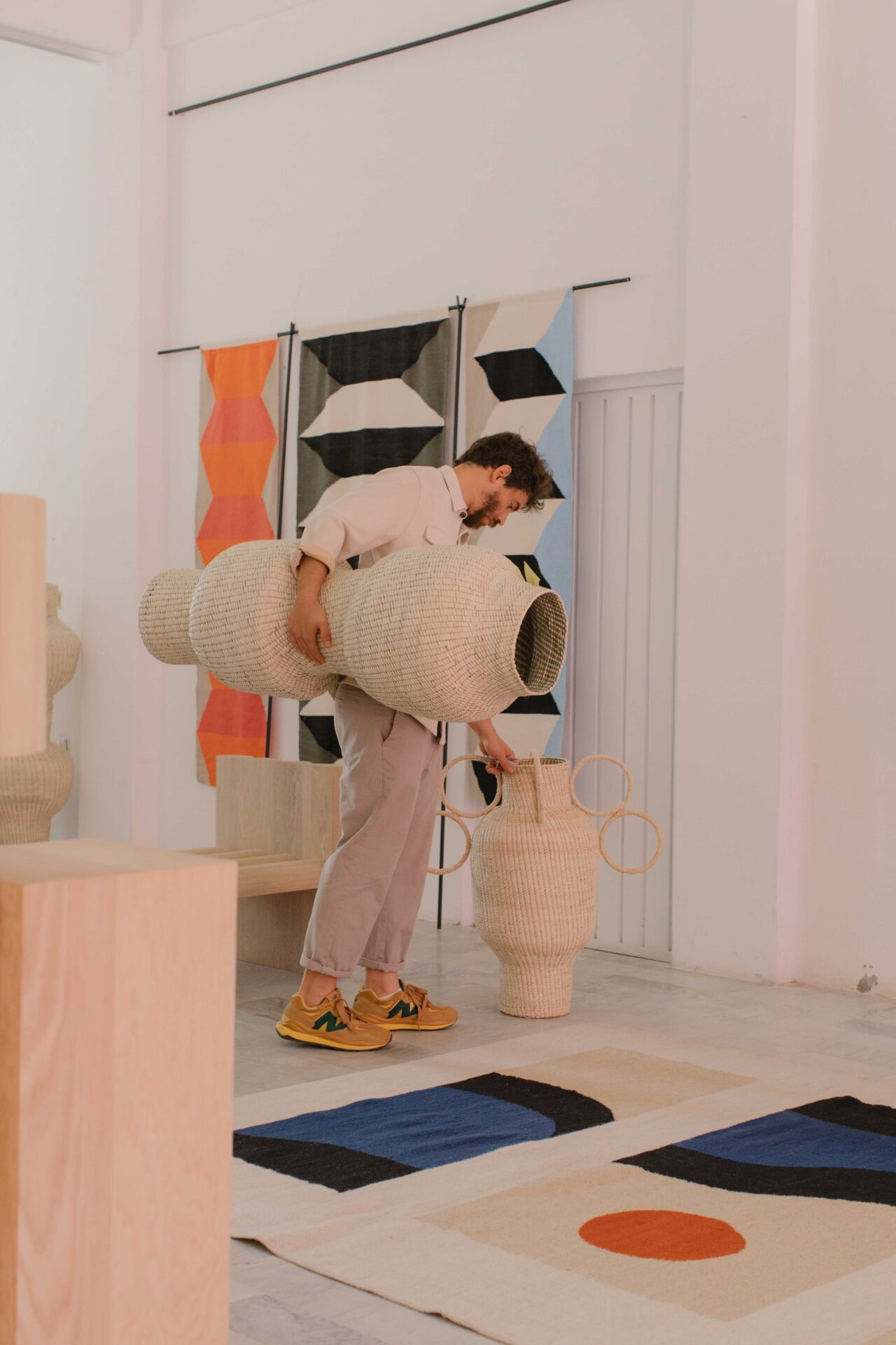 Javier Reyes, rrres studio, Oaxacao | Reyes holds a big woven basket while looking at a woven rug