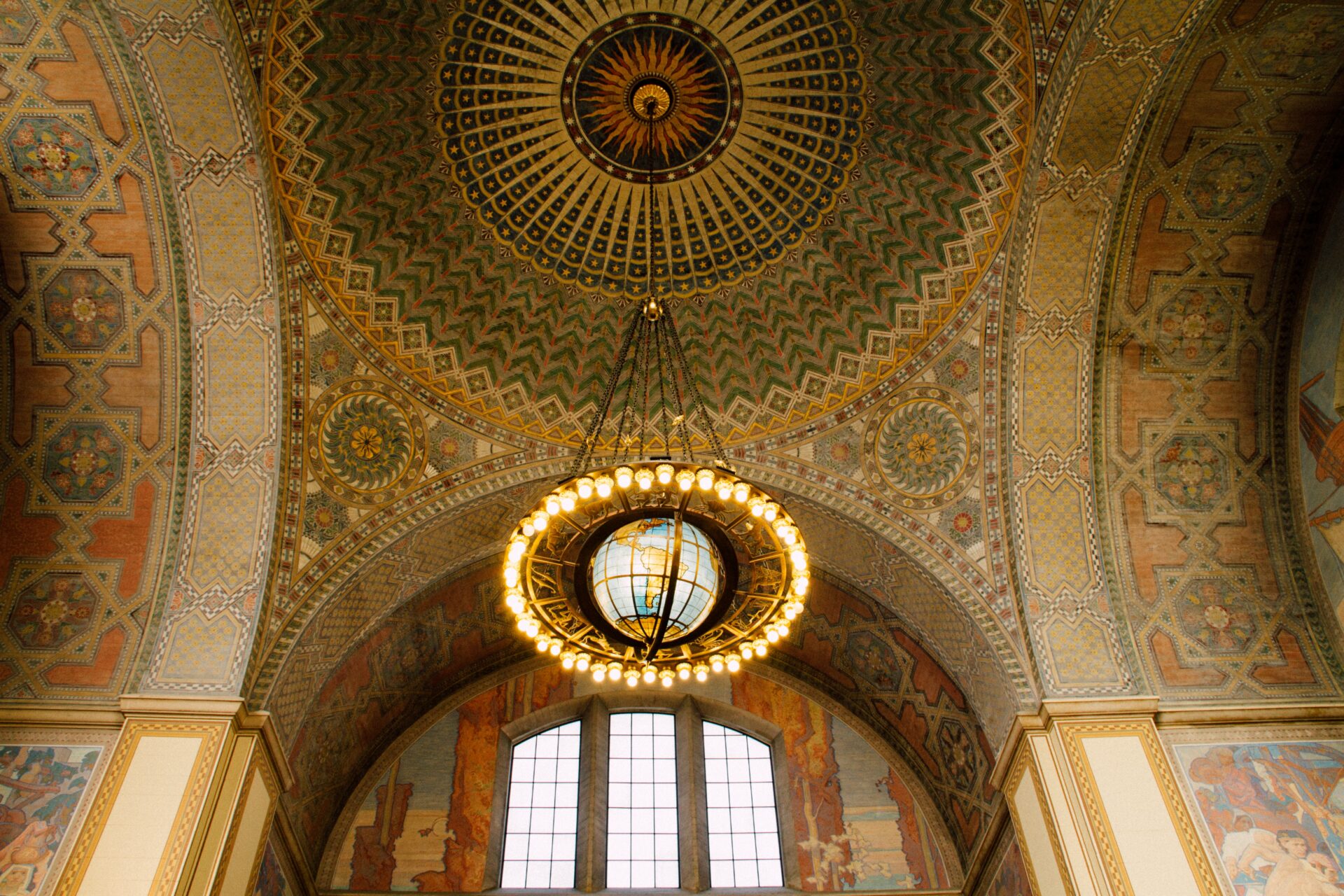 Looking up at the ceiling of LA Union Station, will beautiful mosaics and an art deco light installation of a globe framed by globe lights