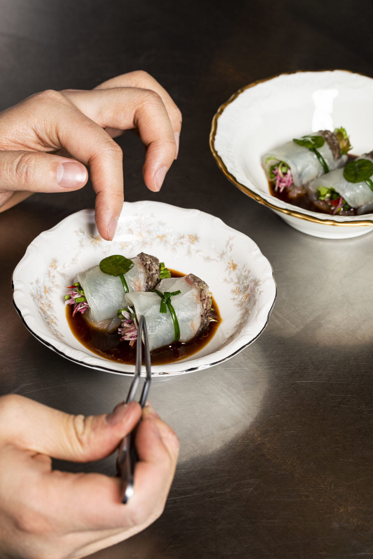 Best restaurants LA Arts District | Plating up at Kato, two hands holding kitchen tweezers gently manoeuvre two delicate rolls into place on shell-shaped plates