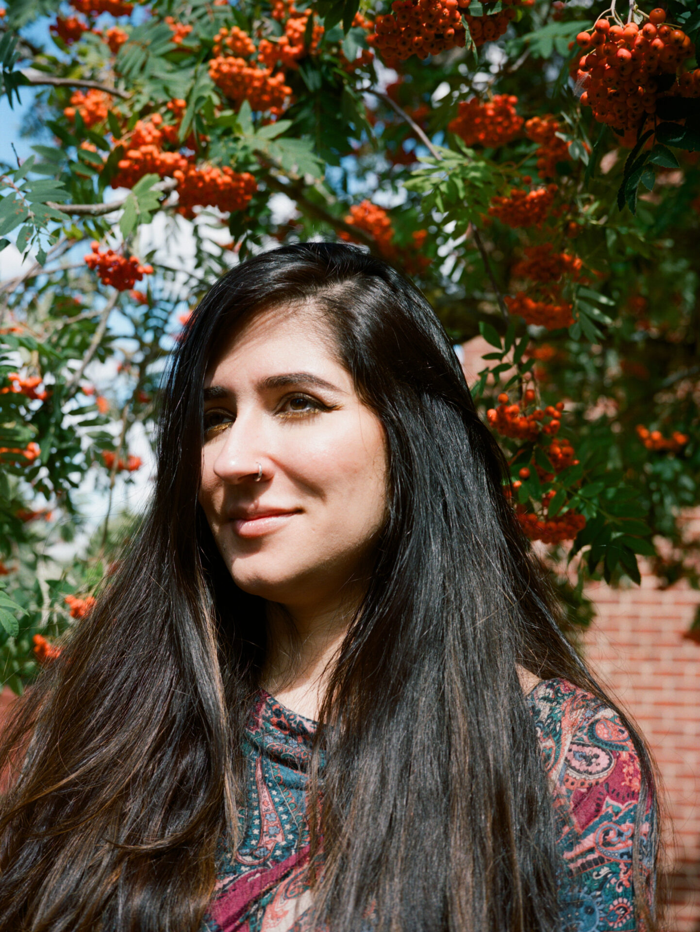 An interview with poet Nikita Gill | A portrait of Nikita Gill, stood beneath a tree with orange berries