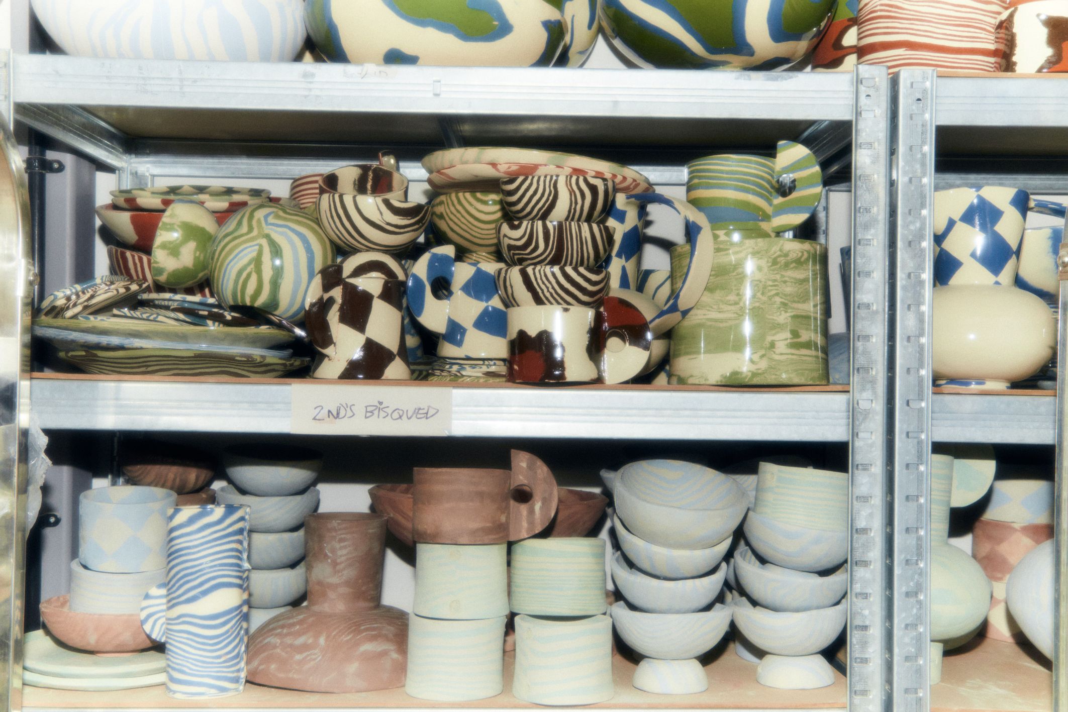 In the studio with Henry Holland | An assortment of bowls, cups, plates and mugs on shelves at various stages of firing.