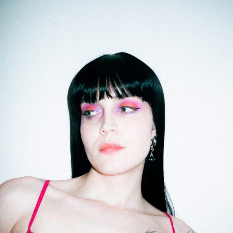 Woman with long black hair wearing pink eyeshadow and pink dress.