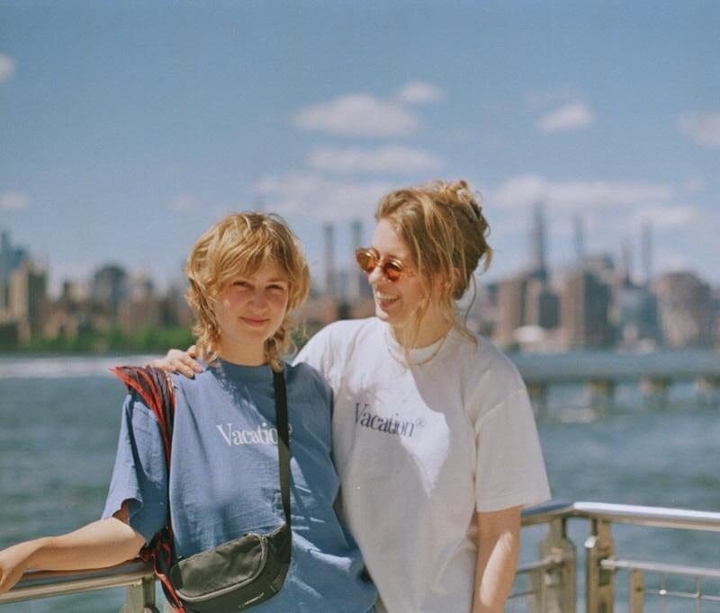 Two people standing in front of a body of water with the view of the city in the background.