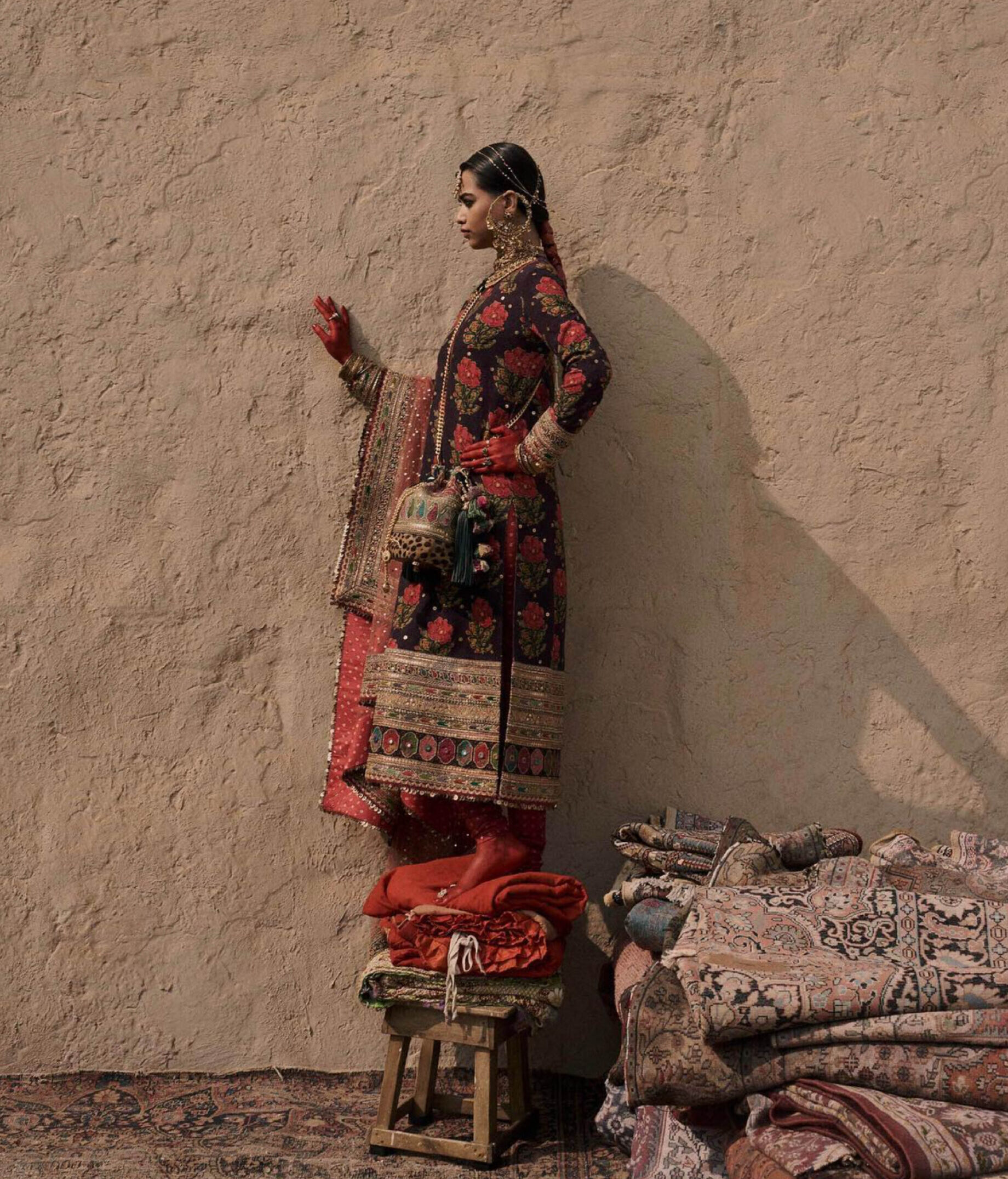 Mumbai fashion designers | A woman dressed in a traditional ensemble standing on a chair on top of rugs.