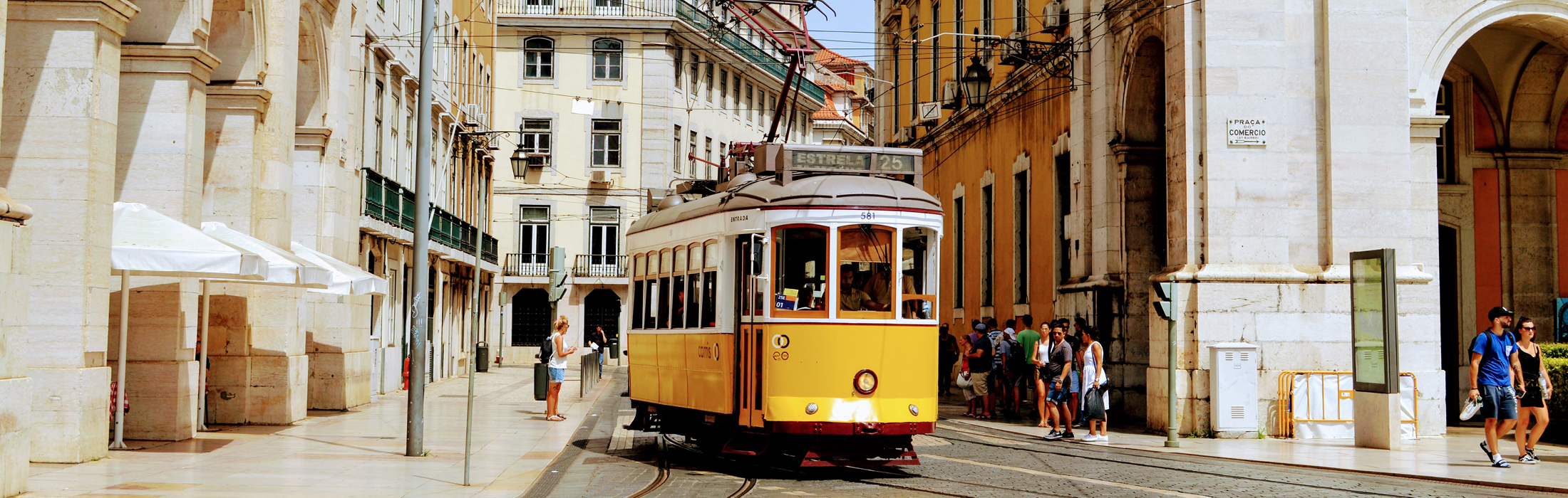 A yellow tram steers through a busy street in Lisbon