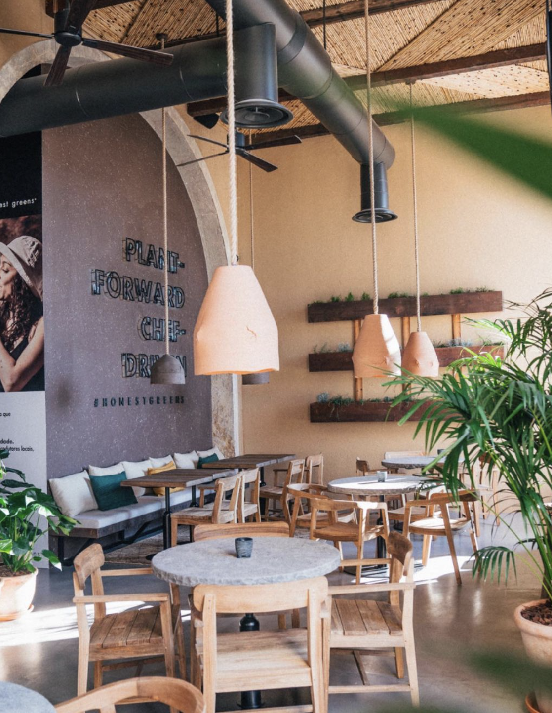 Chairs and round tables beneath pendant lights hanging from a high ceiling.