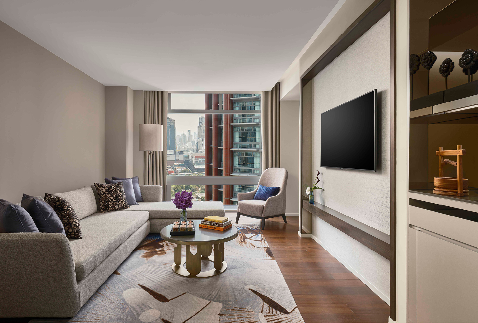 View of window, L shaped sofa, coffee table and flat screen TV in a suite at Chatrium Grand Bangkok