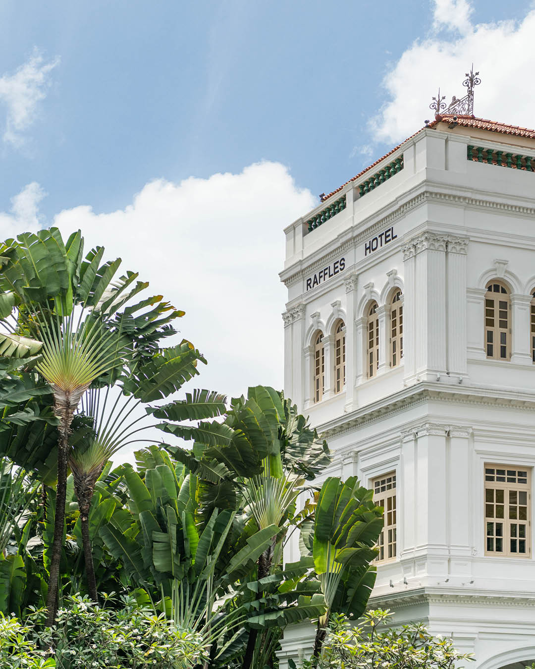 A detail of the exterior of Raffles Singapore, with palm trees and a blue sky visible.