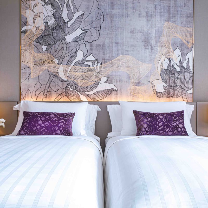 twin beds with luxury white linen, purple pillows and wall art at bedhead in a family suite