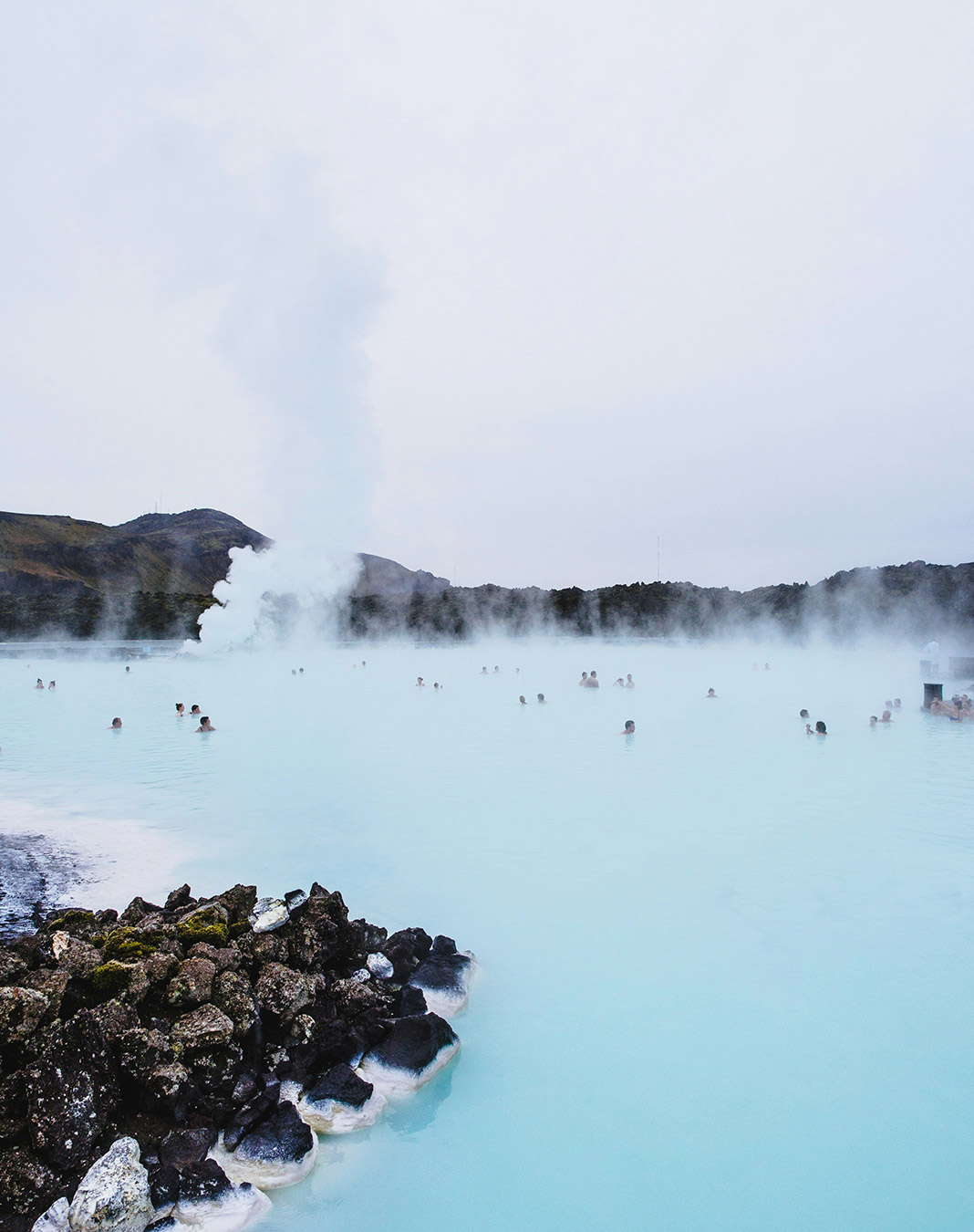 The Blue Lagoon geothermal baths. People swim in ice blue water with a column of steam rising from the surface.