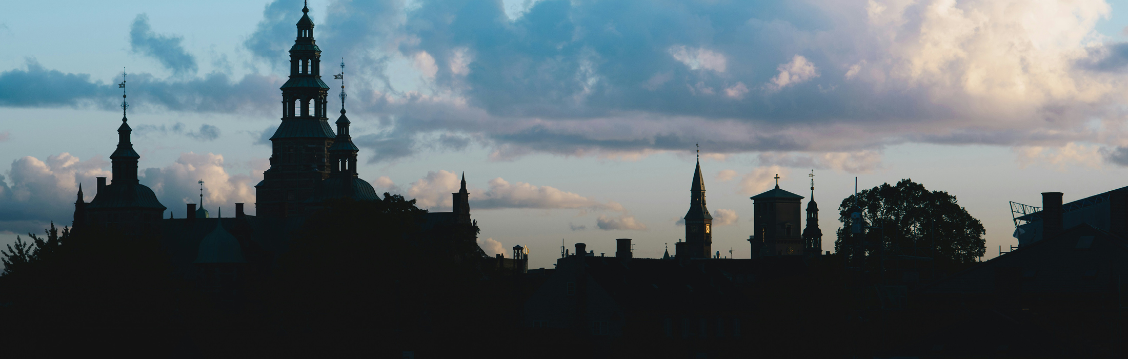 Copenhagen skyline silhouette against a gradient sky with clouds, creating a serene and contemplative mood.