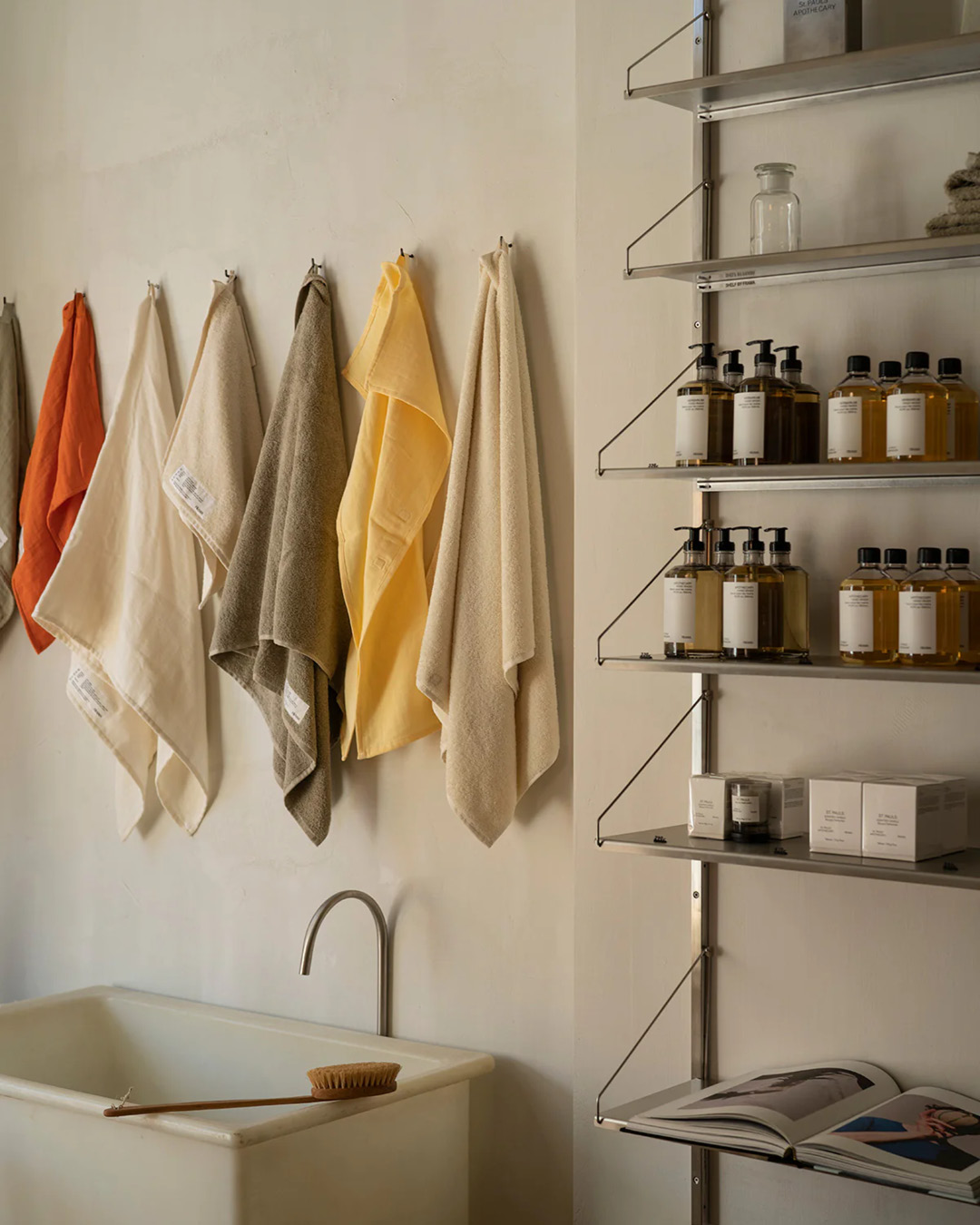 Soaps on a metal shelf next to a small tap and sink with colourful hand towels hanging above in the FRAMA showroom in Copenhagen.