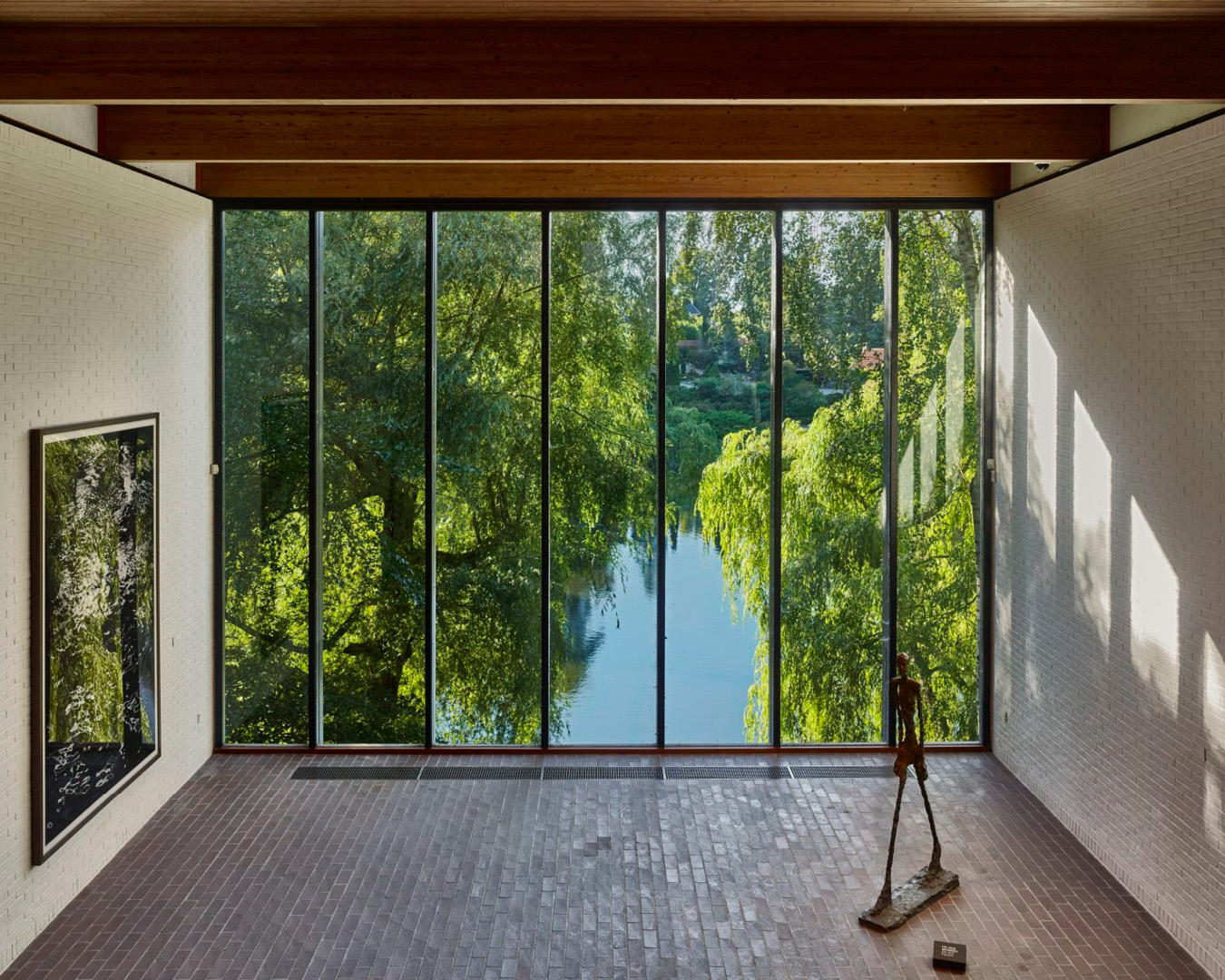 A sculpture by Alberto Giacometti on show at the Louisiana Museum of Modern Art, with a large full size picture window behind it showing a lake and trees.