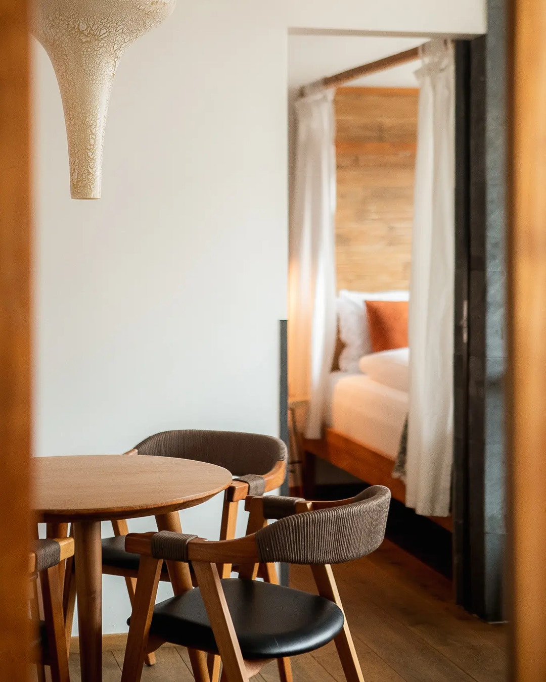 A circular table and chairs framed by pendant lights and a four poster bed