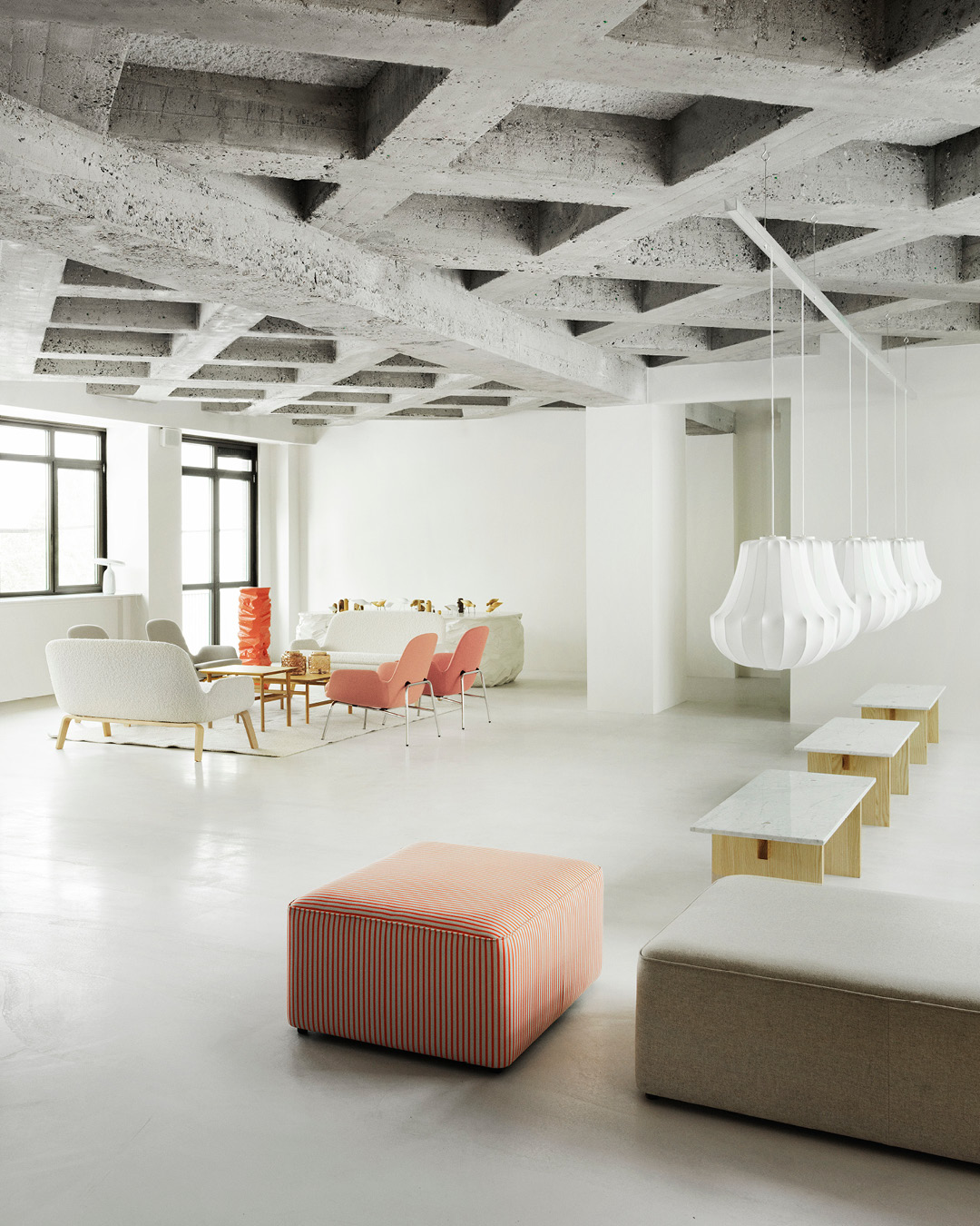 A brutalist concrete ceiling above a polished white floor showroom with design pieces on display at Normann Copenhagen.