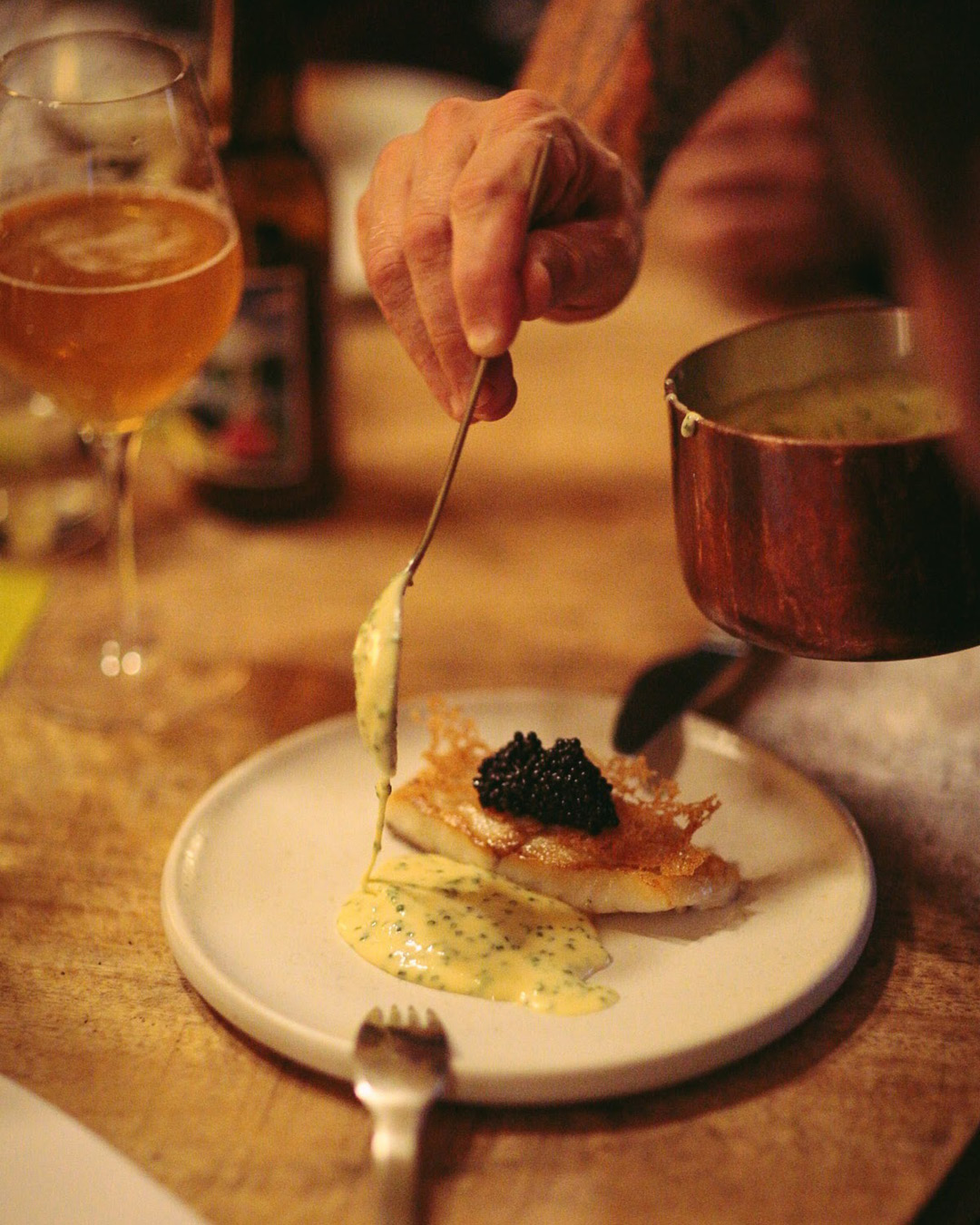 A chef spoons a sauce on a dish at the table at Selma restaurant in Copenhagen.