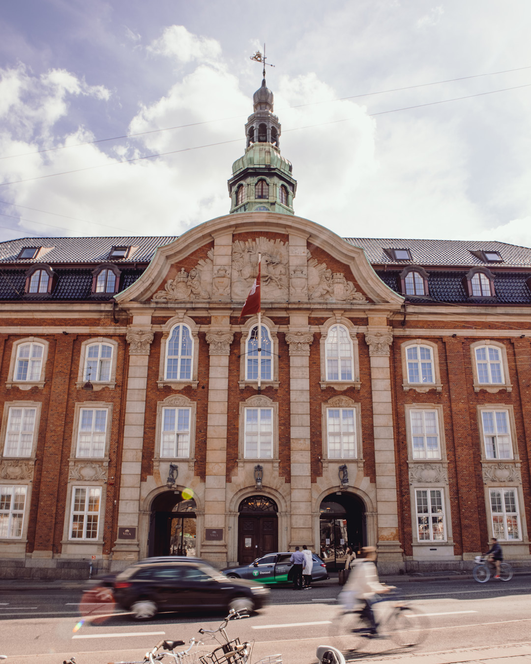 Cyclists and cars whizz past the stately exterior of Villa Copenhagen