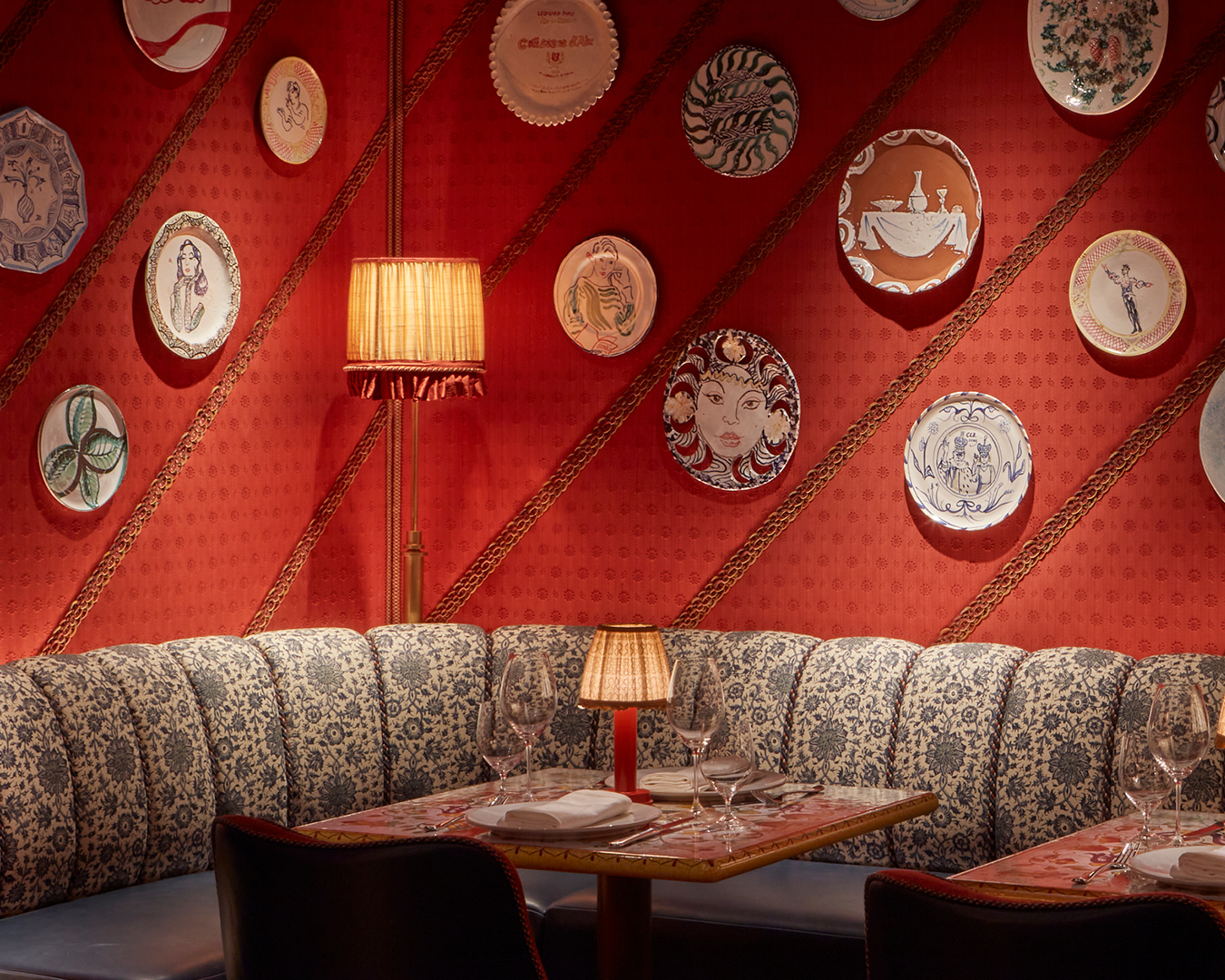 Charming interiors at restaurant Dear Jackie, featuring a cozy banquette, decorative plates on a vibrant red wall, and elegant table settings.