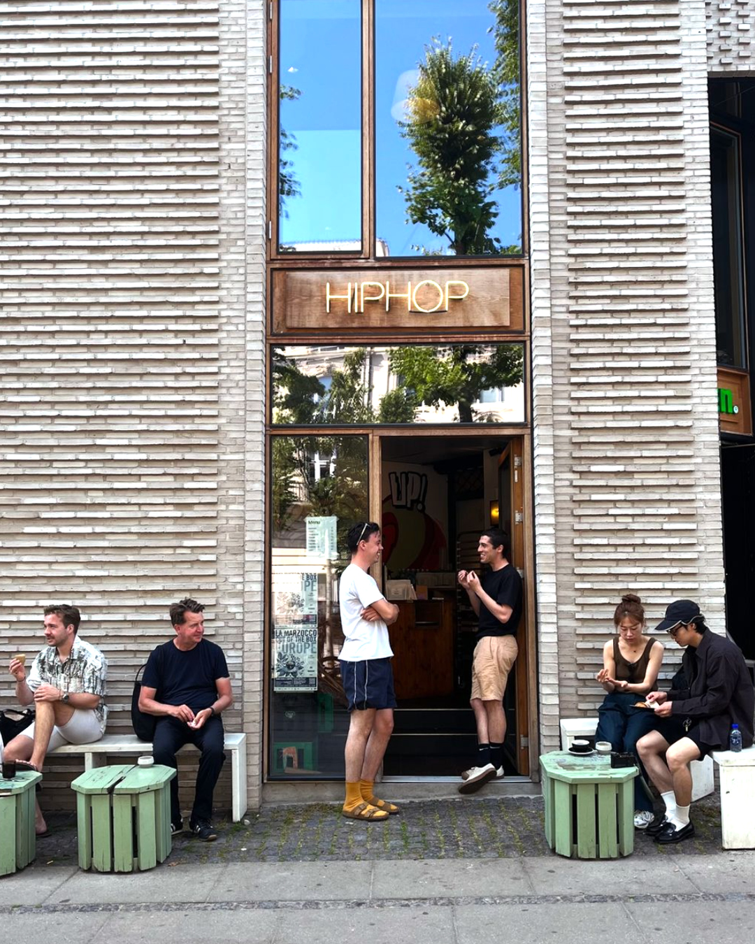 People sit on green stools and white benches outside HipHop coffee shop in Copenhagen.