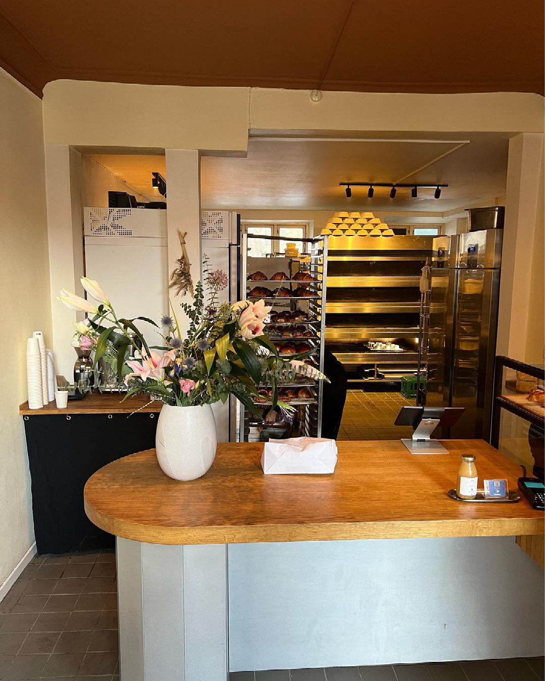 A wooden counter at the front of Bageriet Benji, with glimpses of racks and trays of the bakery itself behind, in Copenhagen.