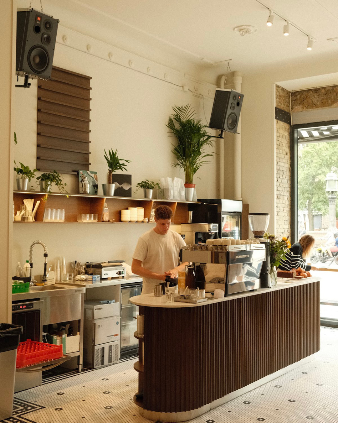 A man works behind the counter at Orsa Coffee shop in Copenhagen, in a high-ceilinged and brightly lit space.