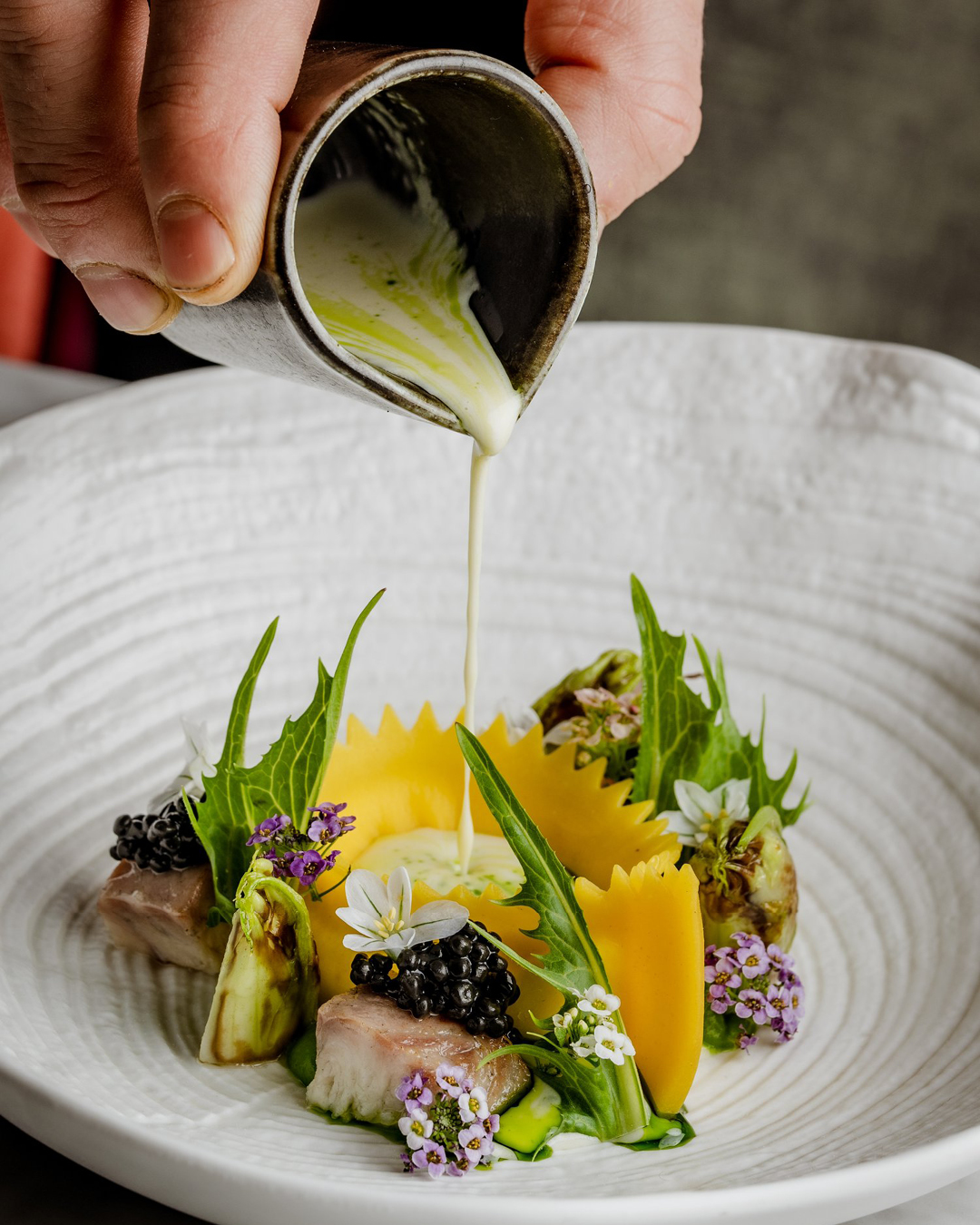 A seasonal plate dressed being dressed in a homemade garnish before serving